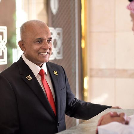 Hotel Intercontinental Dar Al Hijra Madinah By Ihg Medina Exterior foto The photo shows two men engaged in conversation at a hotel reception desk. One man is wearing a dark suit with a red tie and has a welcoming smile. The other man is dressed in traditional attire, possibly a thobe, and a headscarf. The setting appears