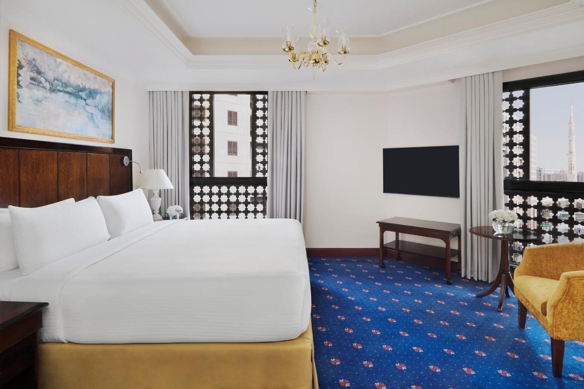 Hotel Intercontinental Dar Al Hijra Madinah By Ihg Medina Exterior foto The photo shows an elegant hotel room. It features a large bed with a white comforter, wooden furniture, and a television mounted on the wall. There are decorative windows with intricate designs that allow natural light to filter in. The floor is cov