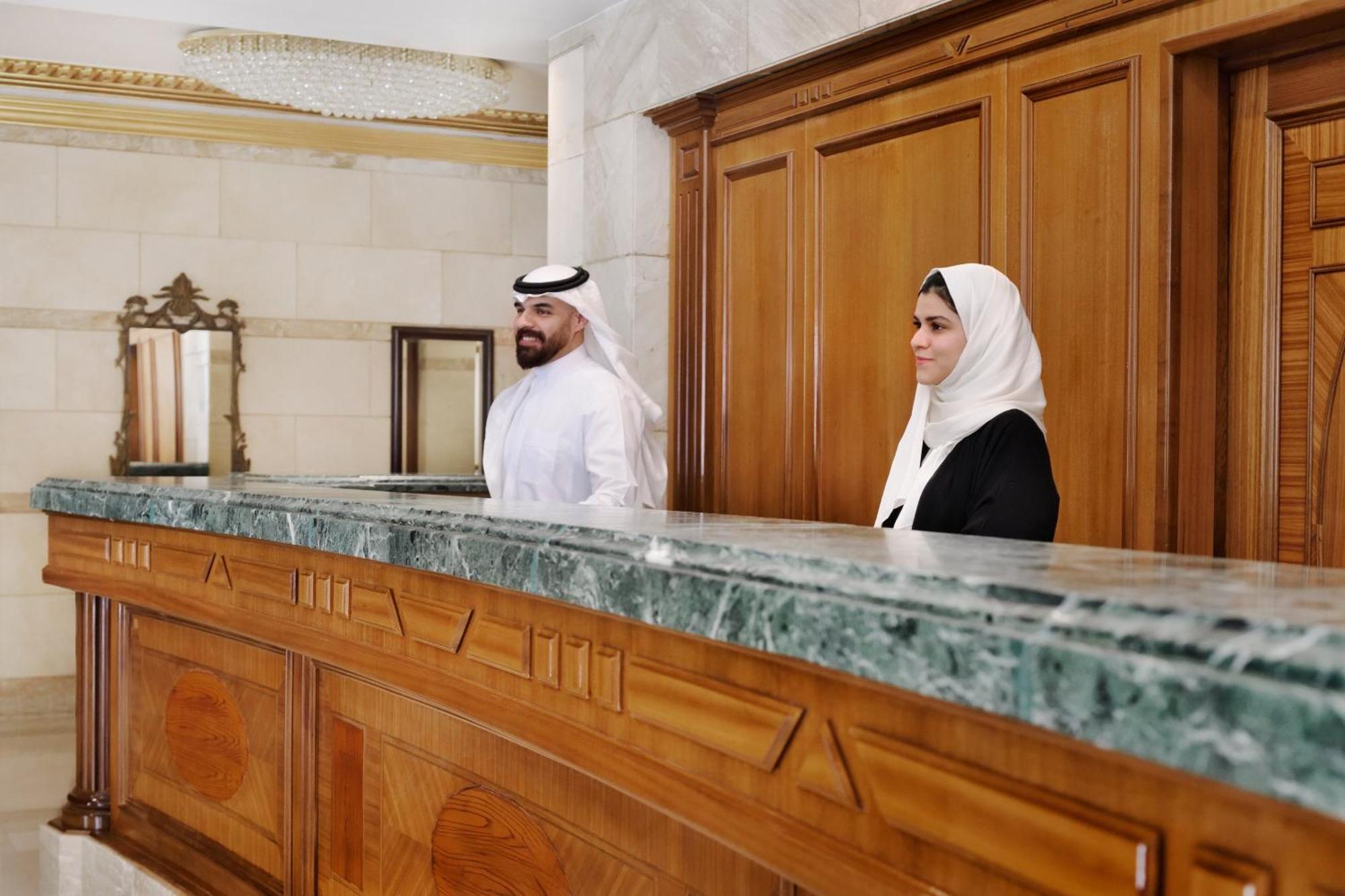 Hotel Intercontinental Dar Al Hijra Madinah By Ihg Medina Exterior foto The photo shows two individuals standing behind a reception or service desk. The desk appears to be made of wood with a green marble top. One of the individuals is wearing a traditional outfit and a headscarf, while the other is dressed in a black ou