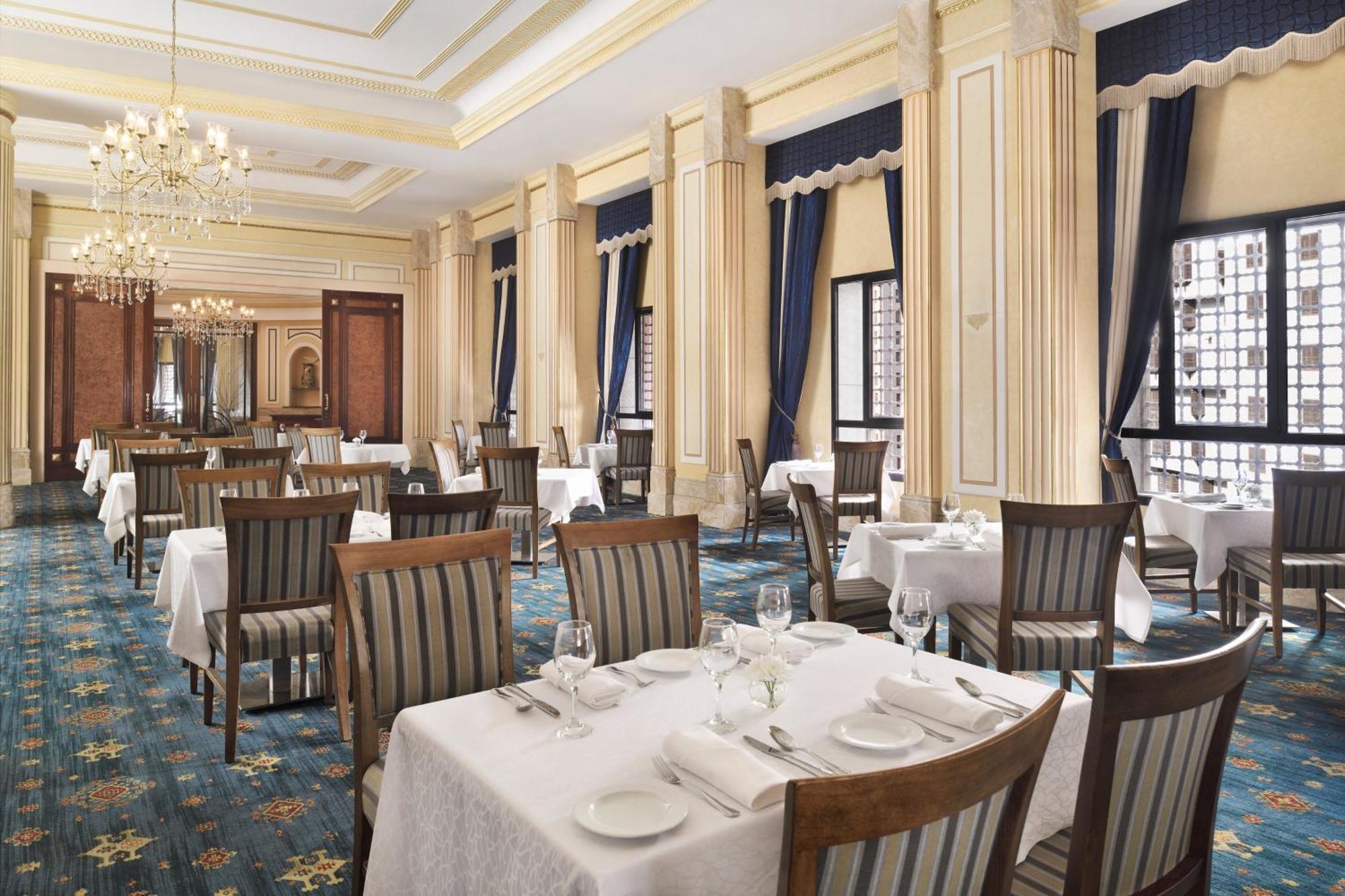 Hotel Intercontinental Dar Al Hijra Madinah By Ihg Medina Exterior foto The photo shows an elegant restaurant interior. It features well-arranged tables covered with white tablecloths, and each table is set with utensils and glassware. The walls are adorned with ornate columns, and tall windows draped with dark blue curt