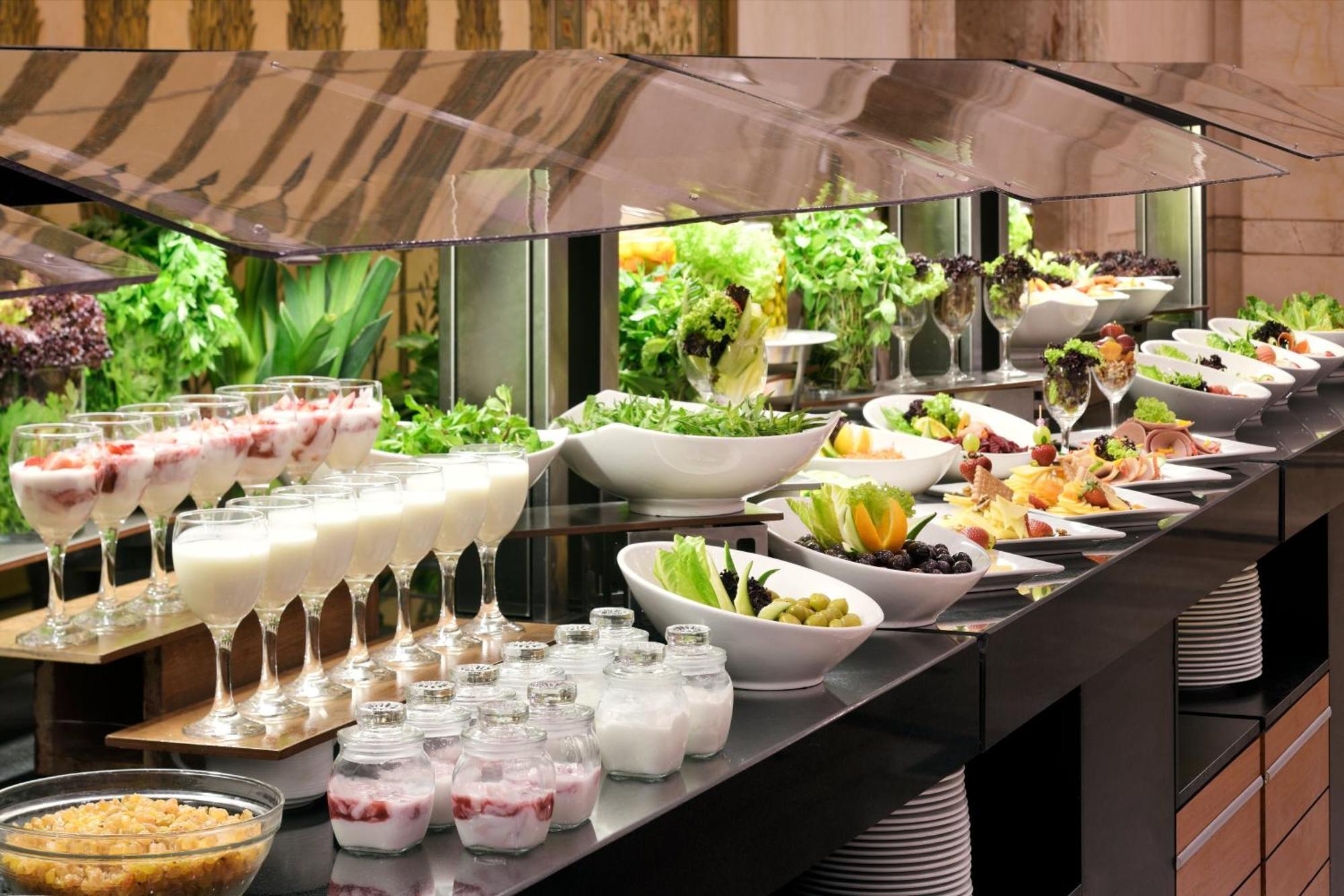 Hotel Intercontinental Dar Al Hijra Madinah By Ihg Medina Exterior foto The photo depicts a buffet-style display of various food items. There are multiple glass bowls and plates arranged neatly on a counter, showcasing a variety of dishes. The offerings include salads, fruits, and desserts. 

In the foreground, there are