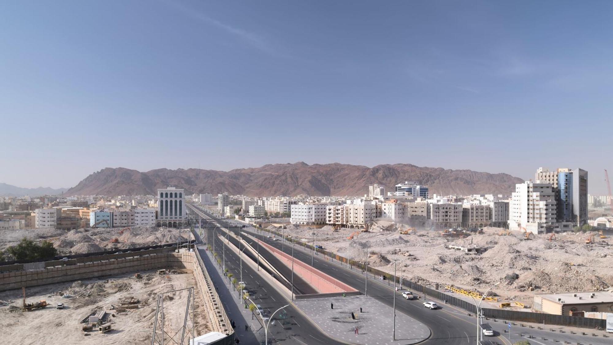 Hotel Intercontinental Dar Al Hijra Madinah By Ihg Medina Exterior foto The photo shows a landscape featuring a wide road that runs through a city. On either side of the road, there are several modern buildings along with some under-construction sites. In the background, there are mountains that rise up, creating a rugge