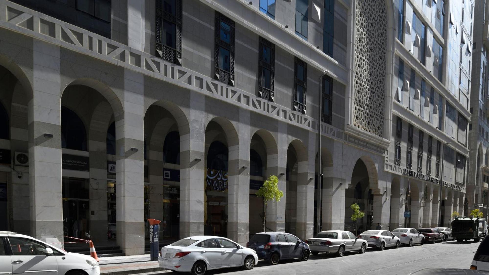 Hotel Intercontinental Dar Al Hijra Madinah By Ihg Medina Exterior foto The photo shows a street scene featuring a modern architectural building with a façade that includes arched columns. The building has a combination of gray and light-colored materials, with rectangular windows. There are several parked cars along the